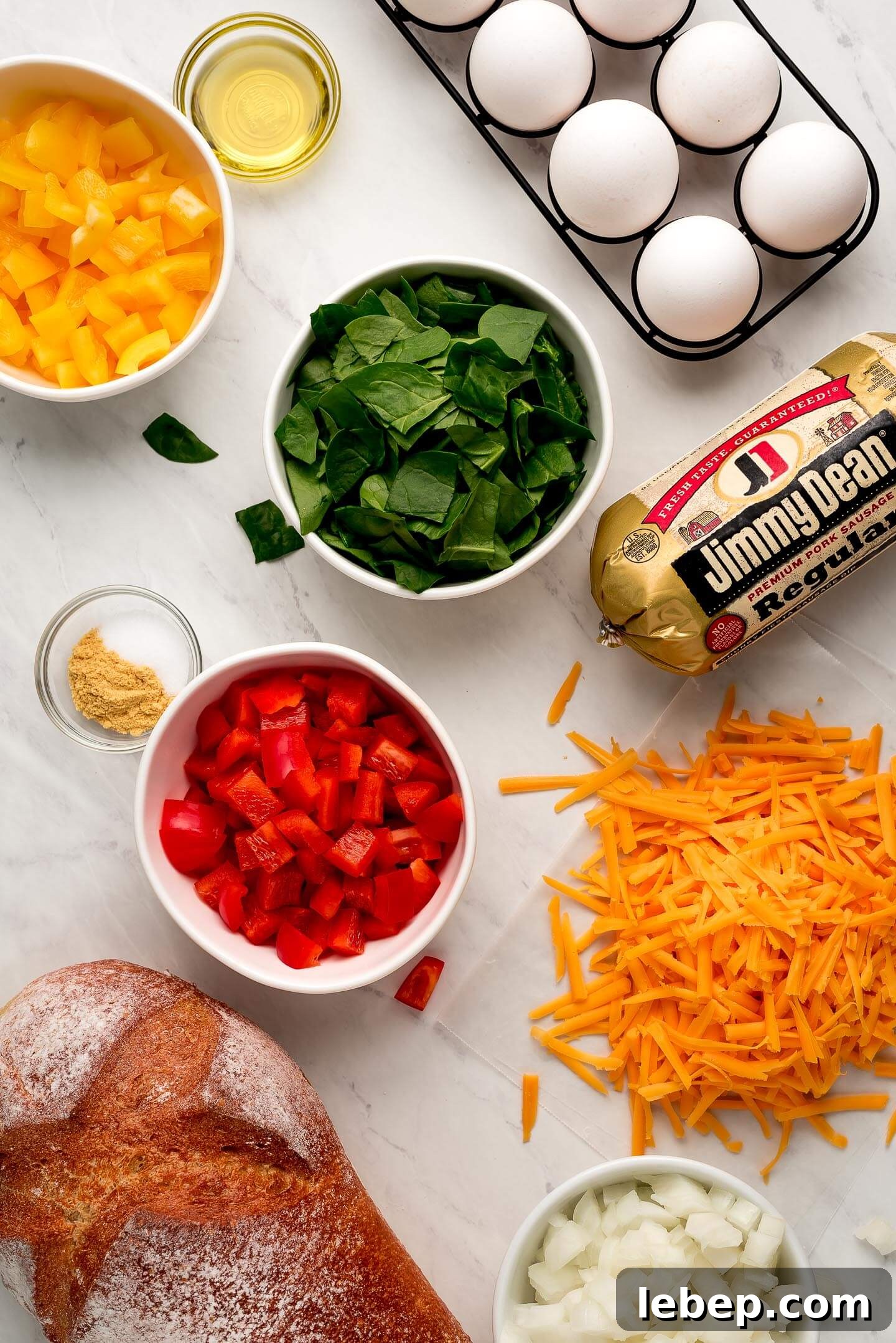 Ingredients on marble surface- eggs, peppers, spinach, sausage, cheese, onions, and bread.