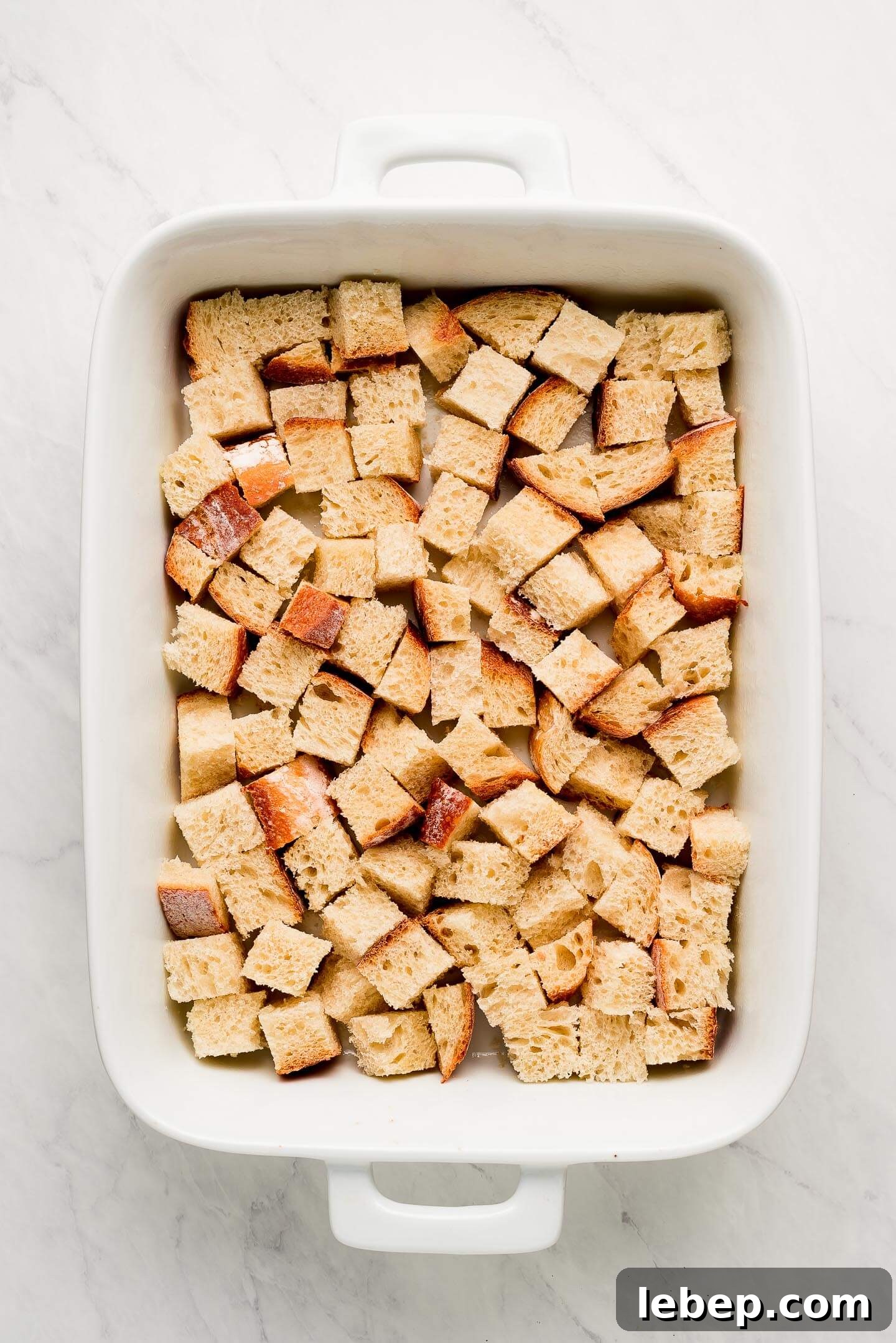 A white baking dish with cubes of bread in the bottom.