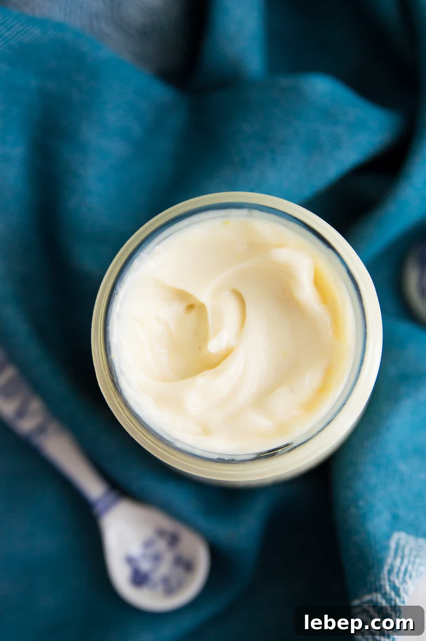 Creamy Immersion Blender Mayonnaise Recipe in Minutes 2 A jar of mayonnaise with a blue tea towel around it.