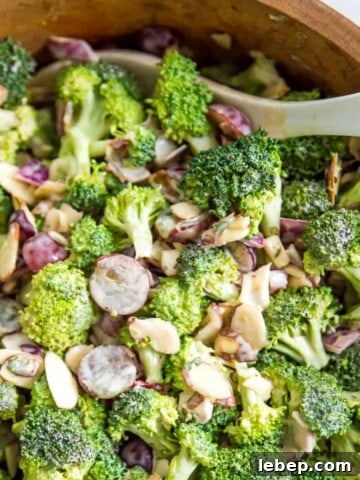 A bowl of healthy broccoli salad with a serving spoon in it.