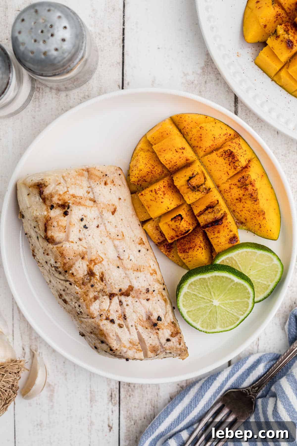 Overhead view of a plate with grilled cobia and mango with lime slices.