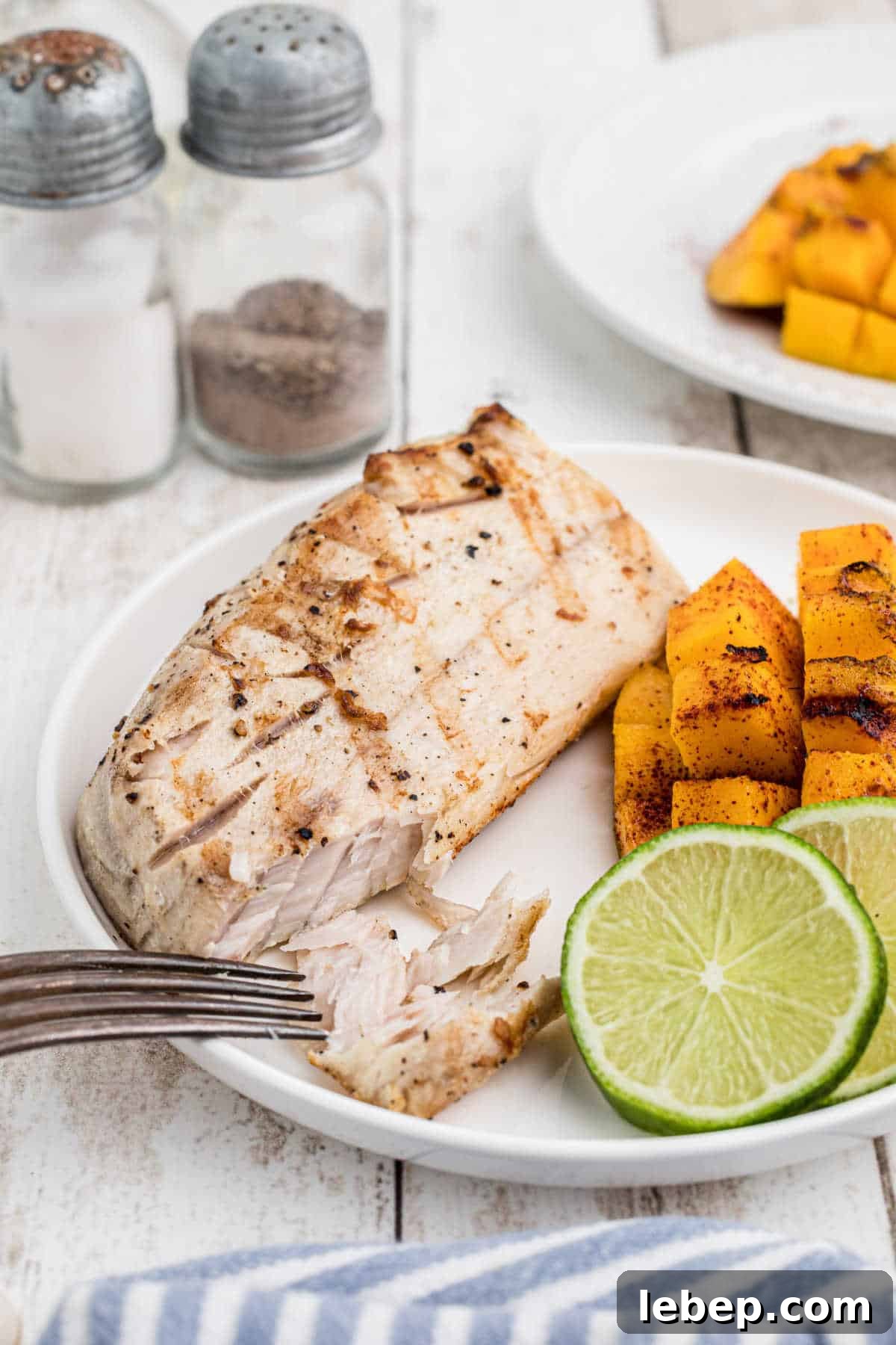Close up of a plate with grilled cobia, mango and lime slices.