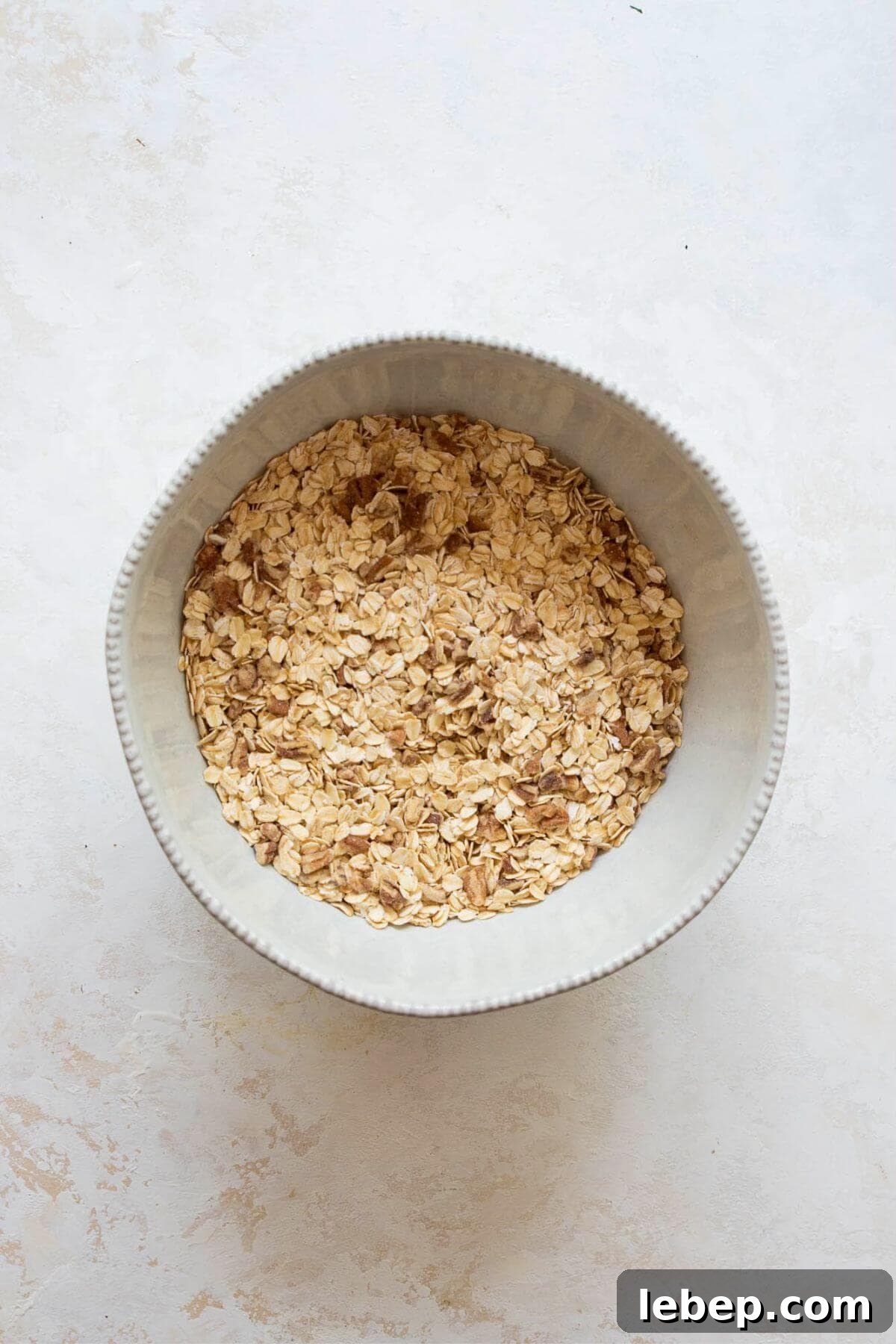 Rolled oats, chopped almonds, and pecans mixed in a white bowl before adding wet ingredients for homemade healthy granola.
