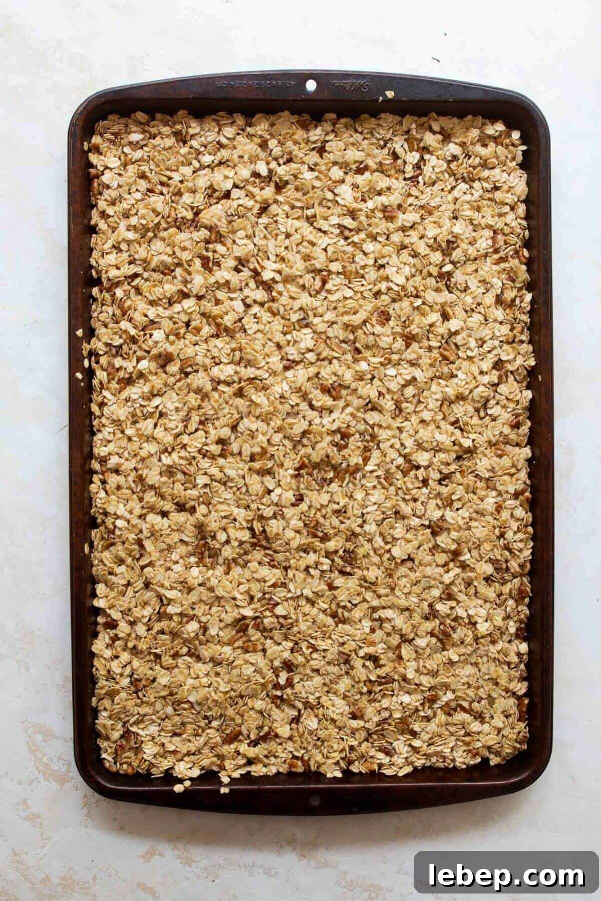 Homemade granola mixture pressed firmly into an even layer on a baking sheet, the key step for chunky clusters.