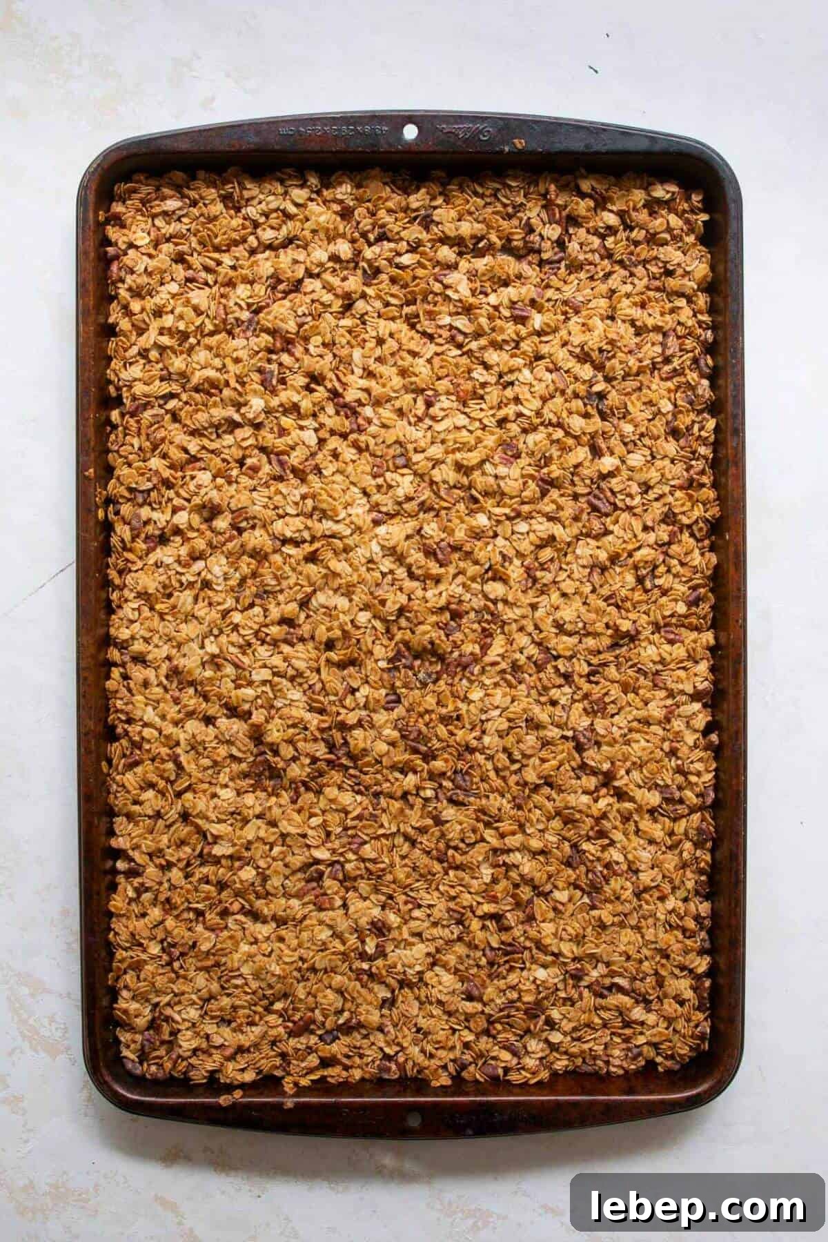 Golden-brown chunky healthy granola fresh out of the oven, cooling on the baking sheet to form clusters.