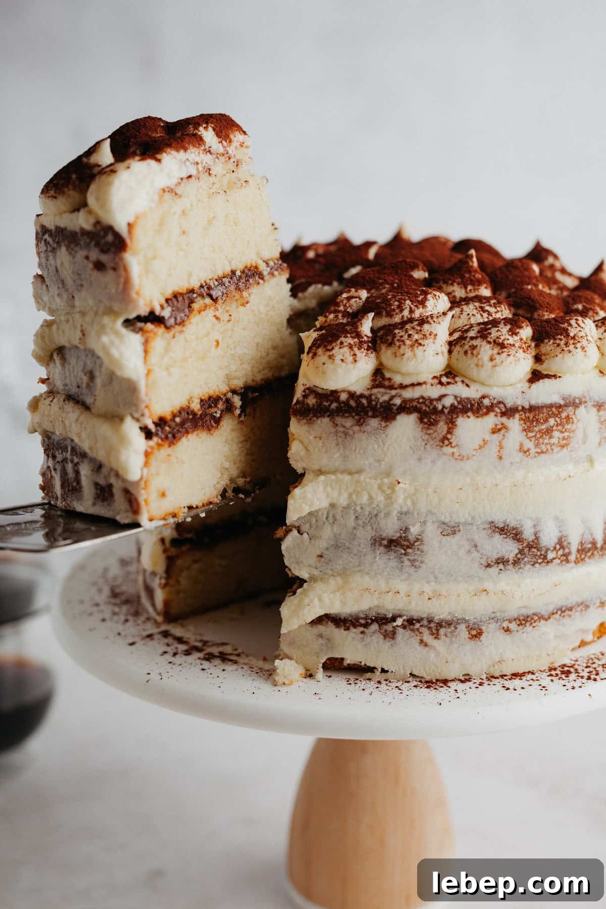 Decadent Tiramisu Layer Cake Recipe for Coffee Lovers 16 Tiramisu layer cake on a cake stand, one slice is being lifted out