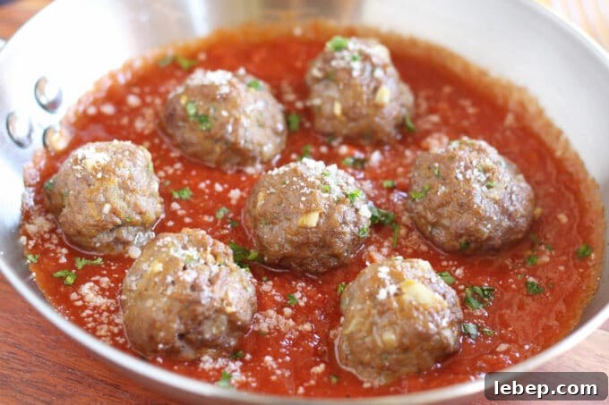 Multiple meatballs in marinara sauce in a steel pan.