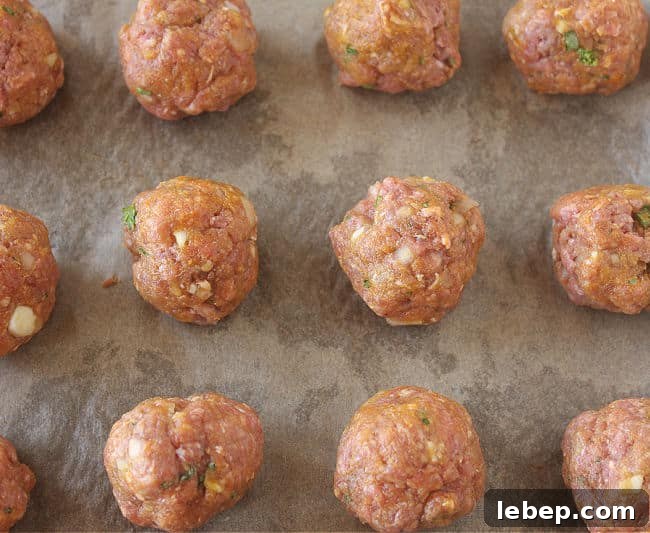 Raw meatballs on a parchment paper-lined baking sheet.