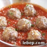 Multiple meatballs in marinara sauce in a steel pan.