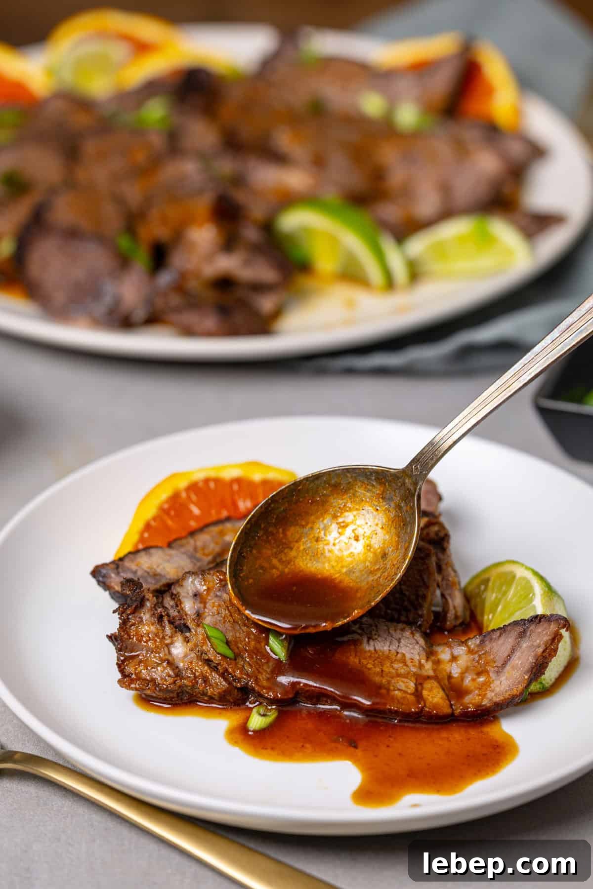 Citrus-Soy Braised Chuck Roast Recipe: Tender, Flavorful Pot Roast 9 A close up of a plate of braised chuck roast with a spoon topping it with a brown sauce.