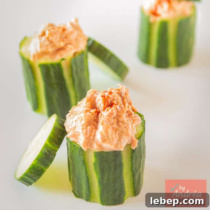 A square photo with three cucumbers filled with tuna salad, with a cucumber cap against it.