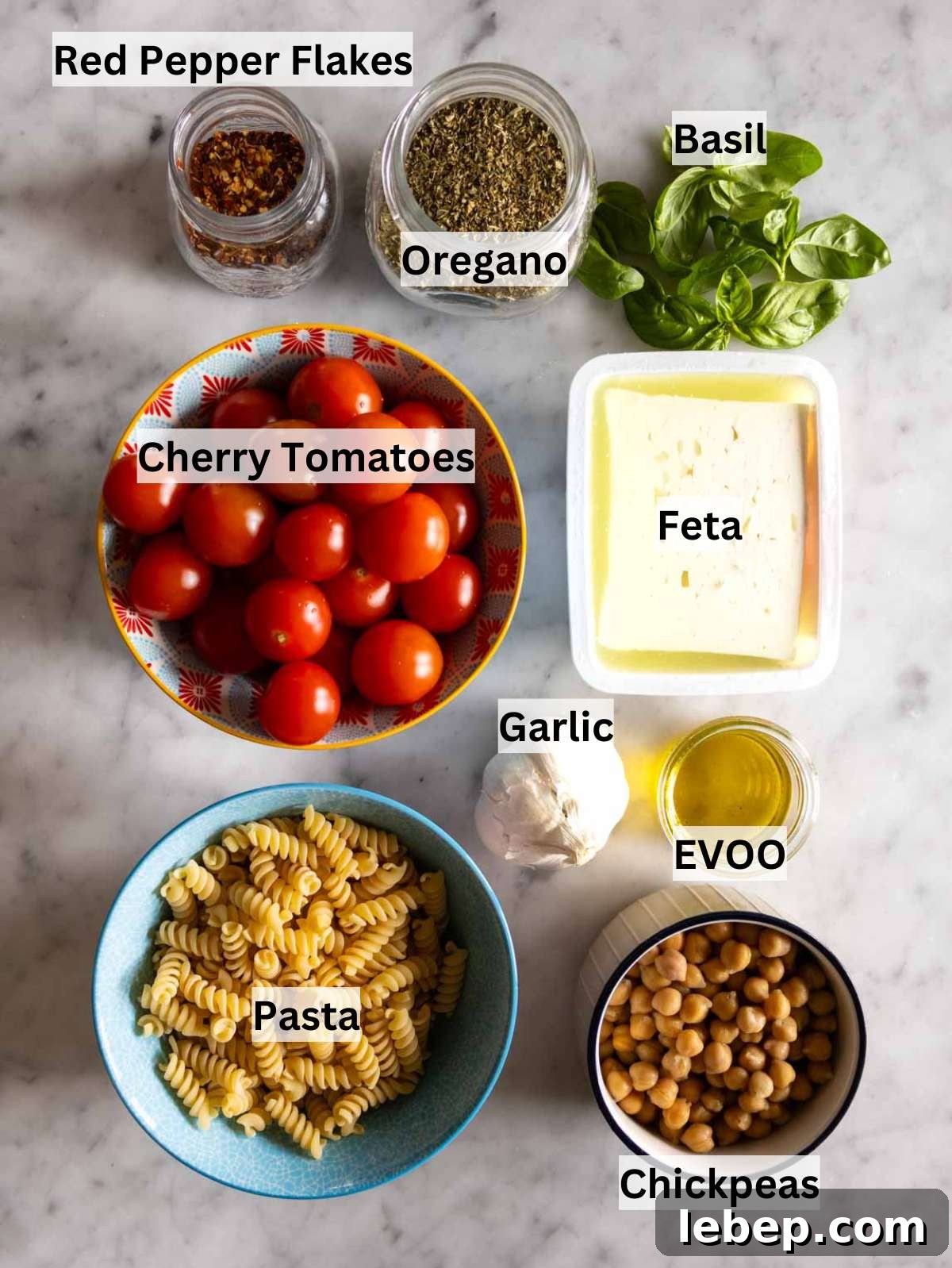 All ingredients for baked feta pasta arranged neatly including feta cherry tomatoes and chickpeas.