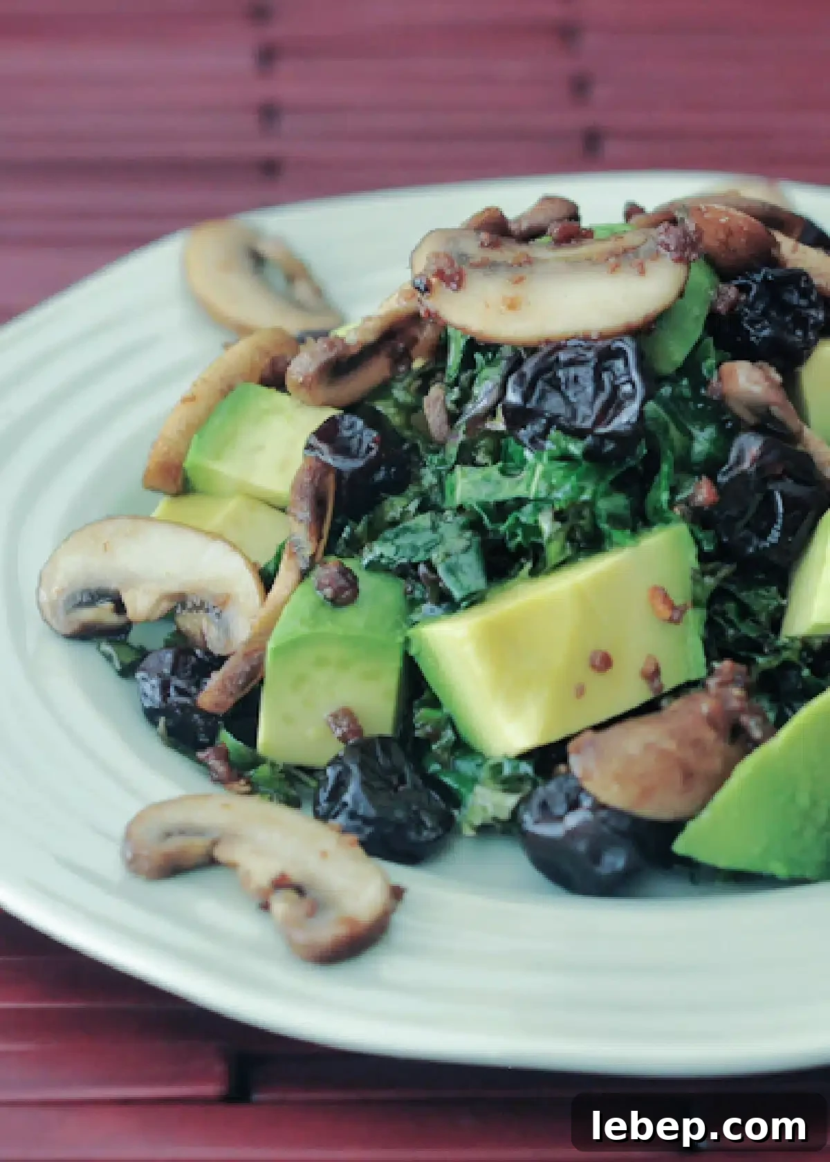 Kale Salad with Warm Bacon Dressing @spabettie #glutenfree #vegan kale salad with warm bacon dressing is kale, cubed avocado, bacon flavored mushrooms on a light green plate with a reddish brown wooden slats placemat.