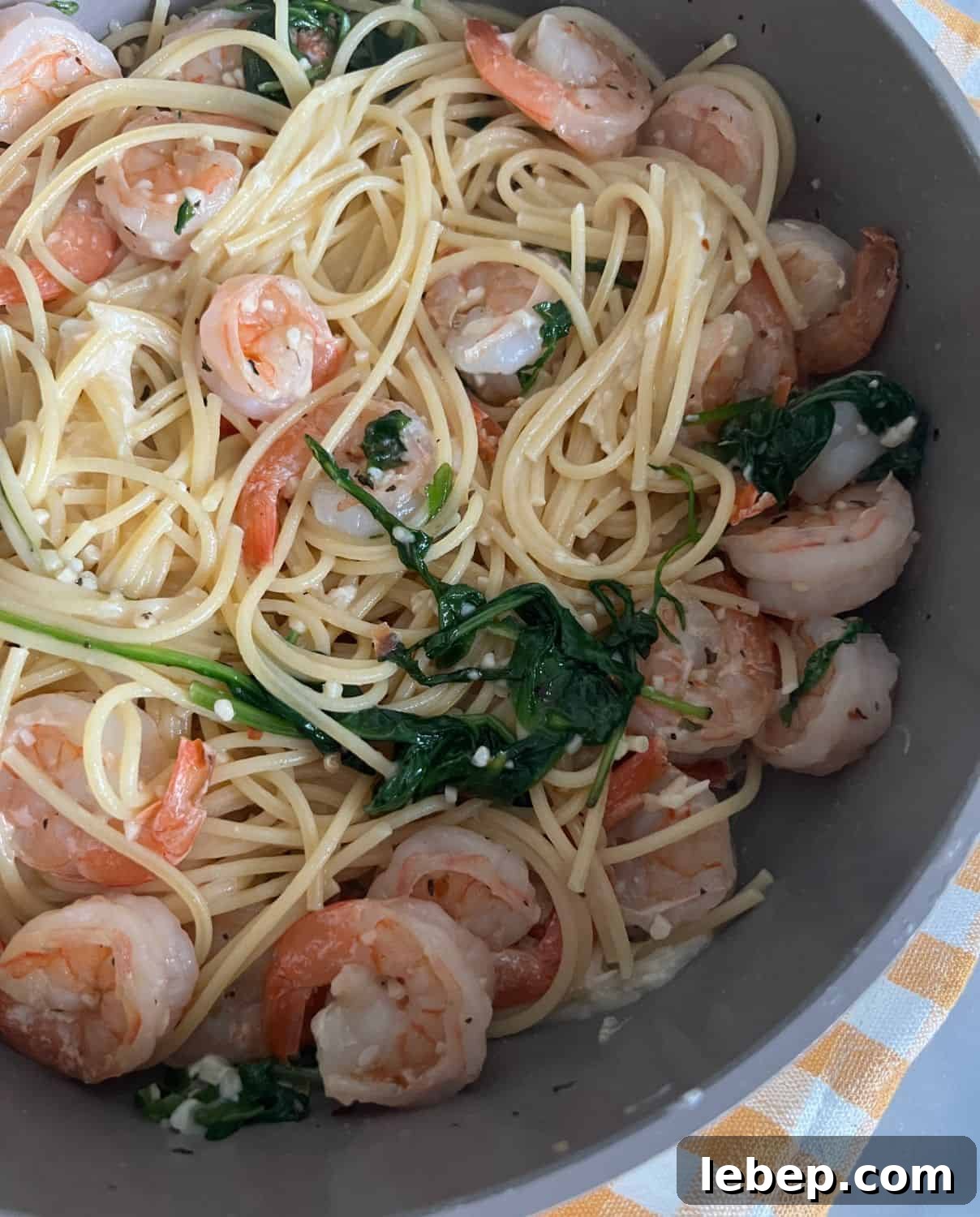 One-Pot Lemon Garlic Shrimp Pasta Recipe 2 Finished one pot lemon garlic shrimp pasta with spinach in a skillet on top of a yellow checkered napkin.