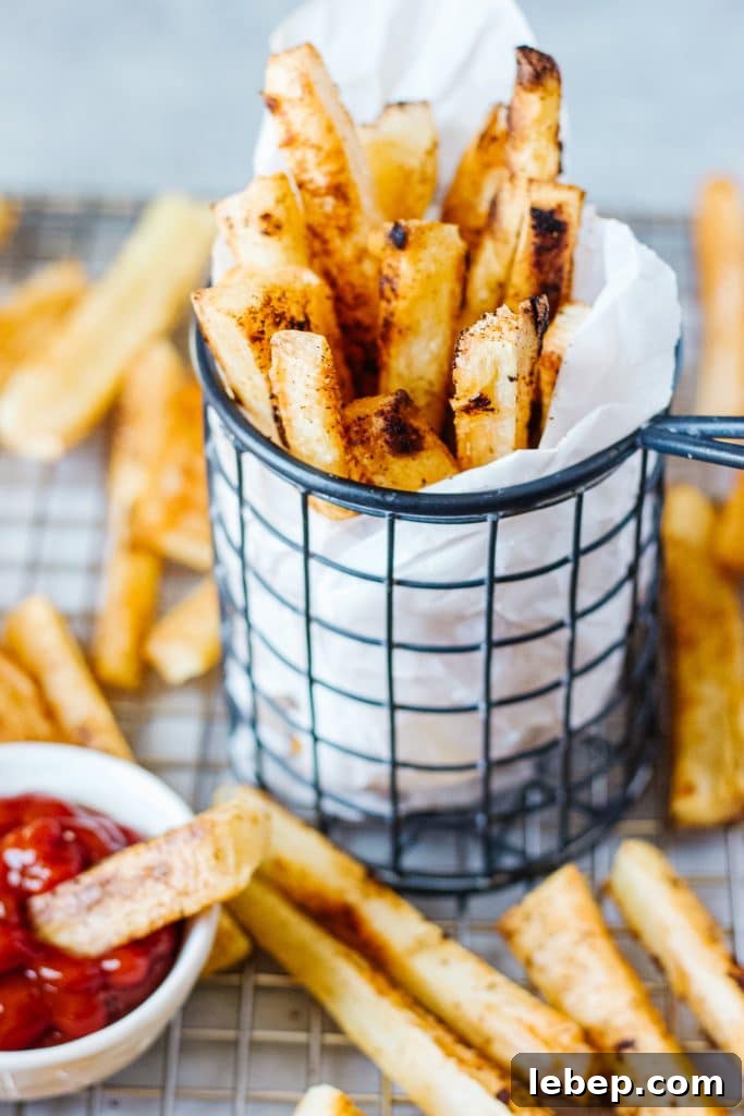 Slices of baked yuca in a cooling rack and in a  wire mesh container with a small container of ketchup and a small piece of the fries in it
