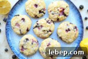 A plate of blueberry muffin cookies with a half of lemon and a whole lemon in opposite corners and blueberries scattered around the plate.