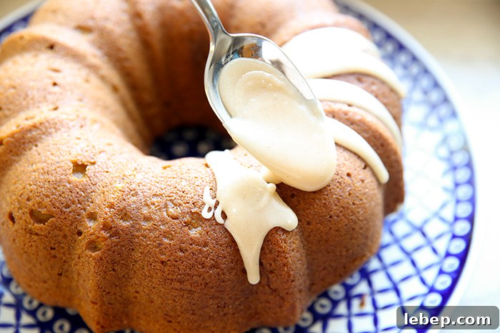 Pumpkin spice bundt cake on a round large Polish potter platter with a spoon held above placing brown butter icing on it.