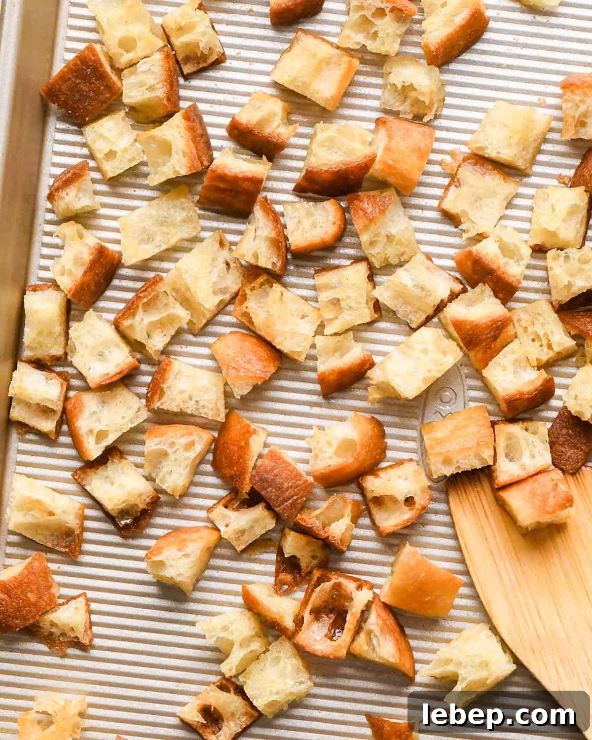 Homemade Croutons on a baking sheet with a wooden spatula