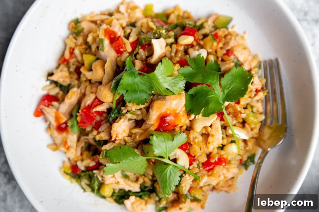 Salmon fried rice in a bowl, drizzled with chili sauce and topped with cilantro sprigs. 