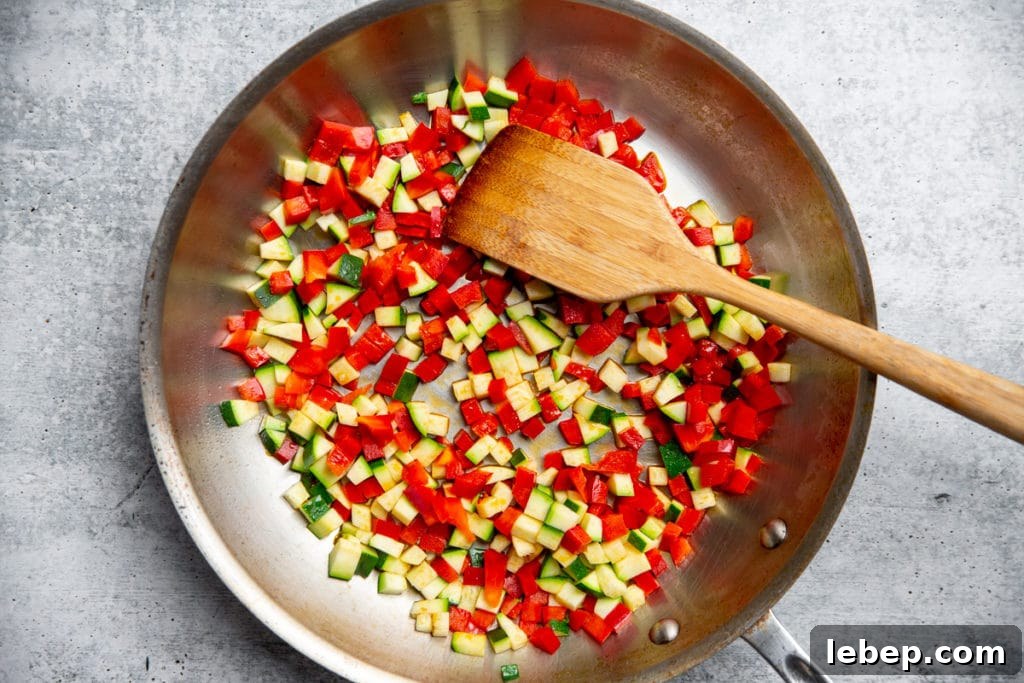 Process shot showing pepper and zucchini cooking in a large skillet. 