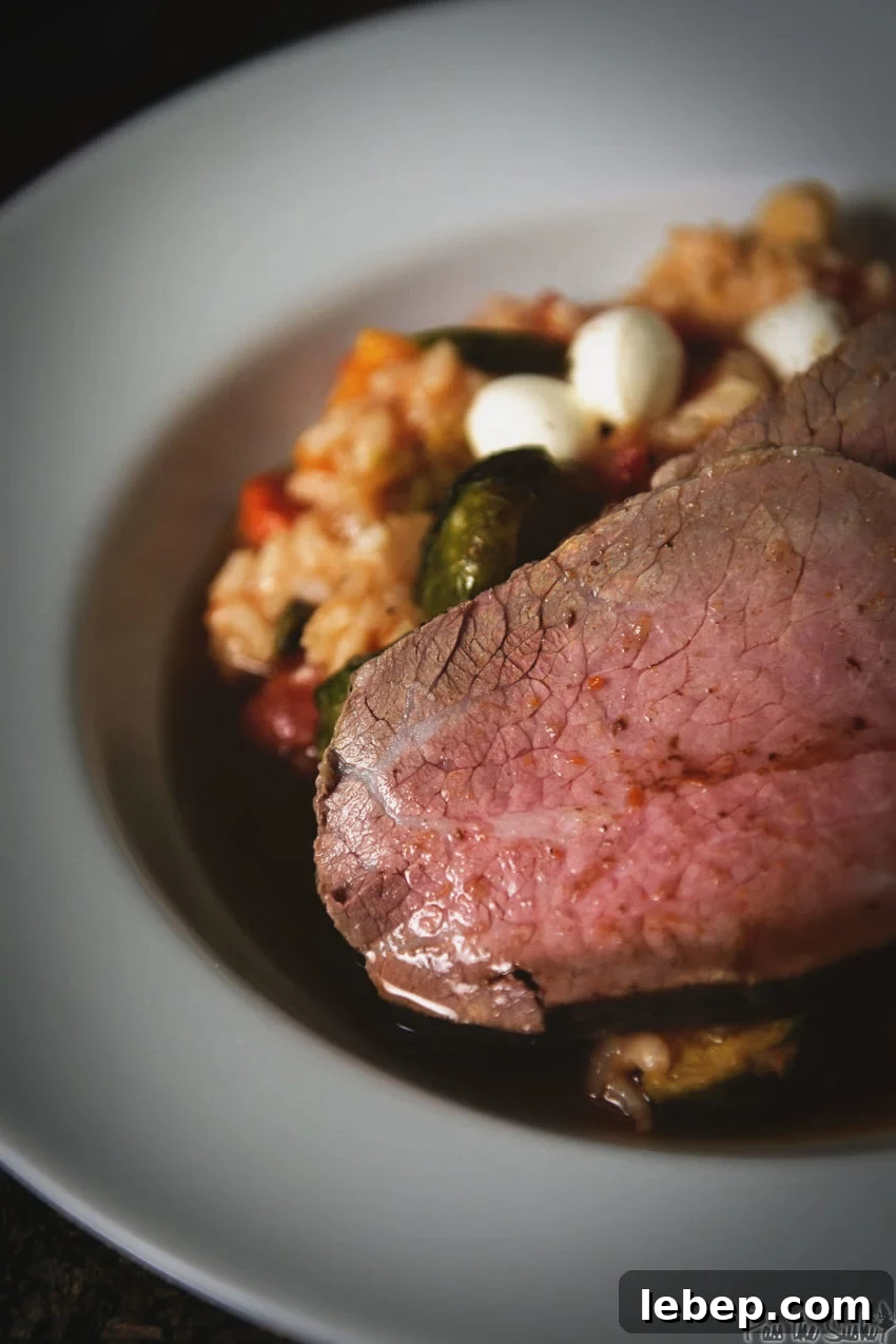 Tender Melt-in-Your-Mouth Eye of Round Roast Recipe 9 Sliced eye round roast on a white platter over risotto