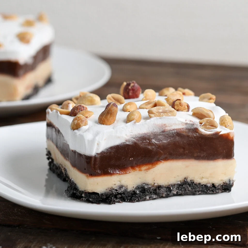 A square slice of Gluten and Dairy Free Oreo Peanut Butter Pie features a dark cookie crust, creamy peanut butter layer, chocolate pudding, whipped topping, and peanuts on top, served on a white plate with another piece blurred in the background.