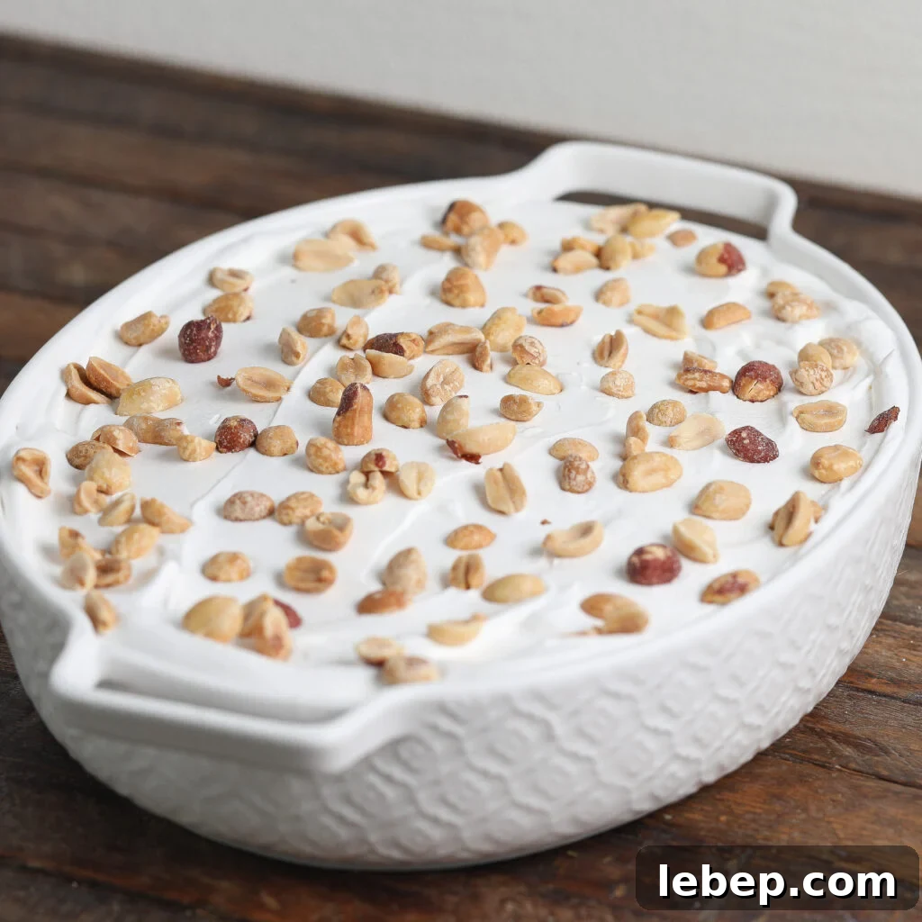 A white ceramic dish filled with a creamy Gluten and Dairy Free Oreo Peanut Butter Pie, topped with a layer of mixed nuts, sits on a wooden surface.