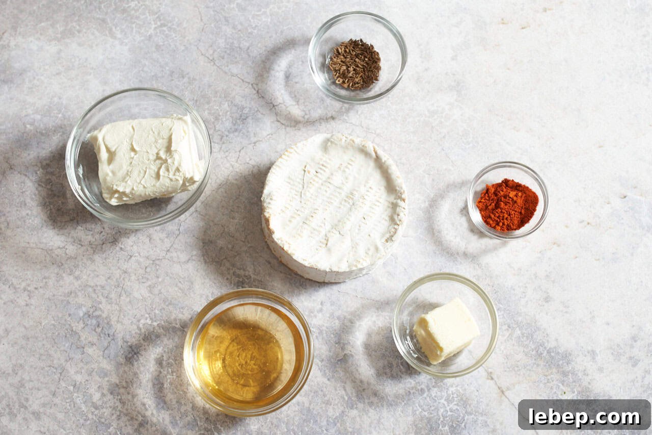 A wheel of camembert cheese surrounded by small bowls of cream cheese, beer, butter, caraway seeds, and paprika.