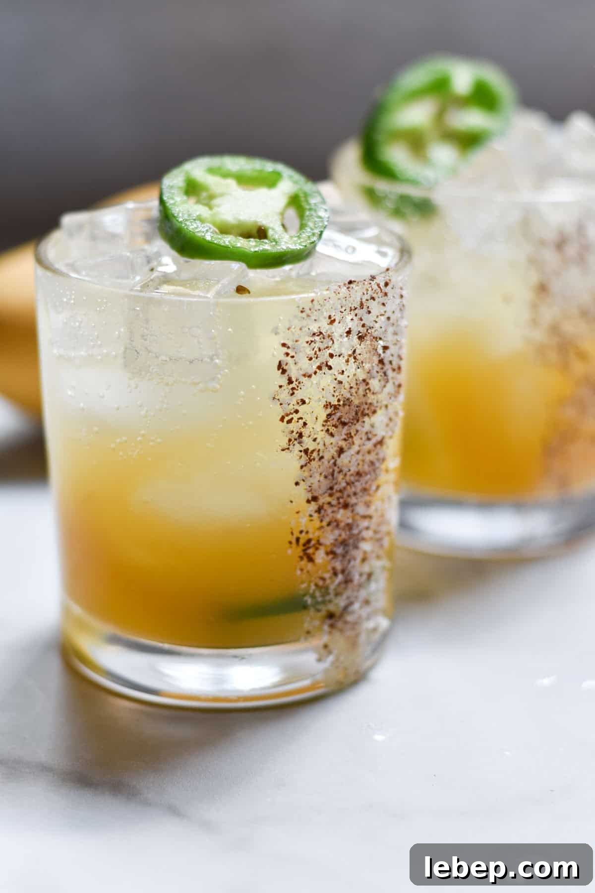 Two margarita mocktails topped with jalapeno slices on a white table.