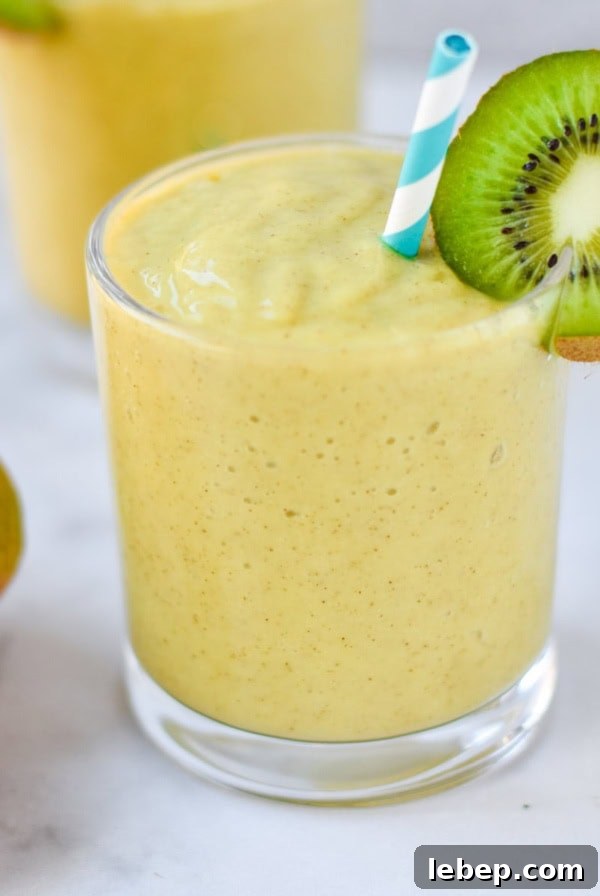 A mango smoothie in a clear glass with a kiwi and blue striped straw.