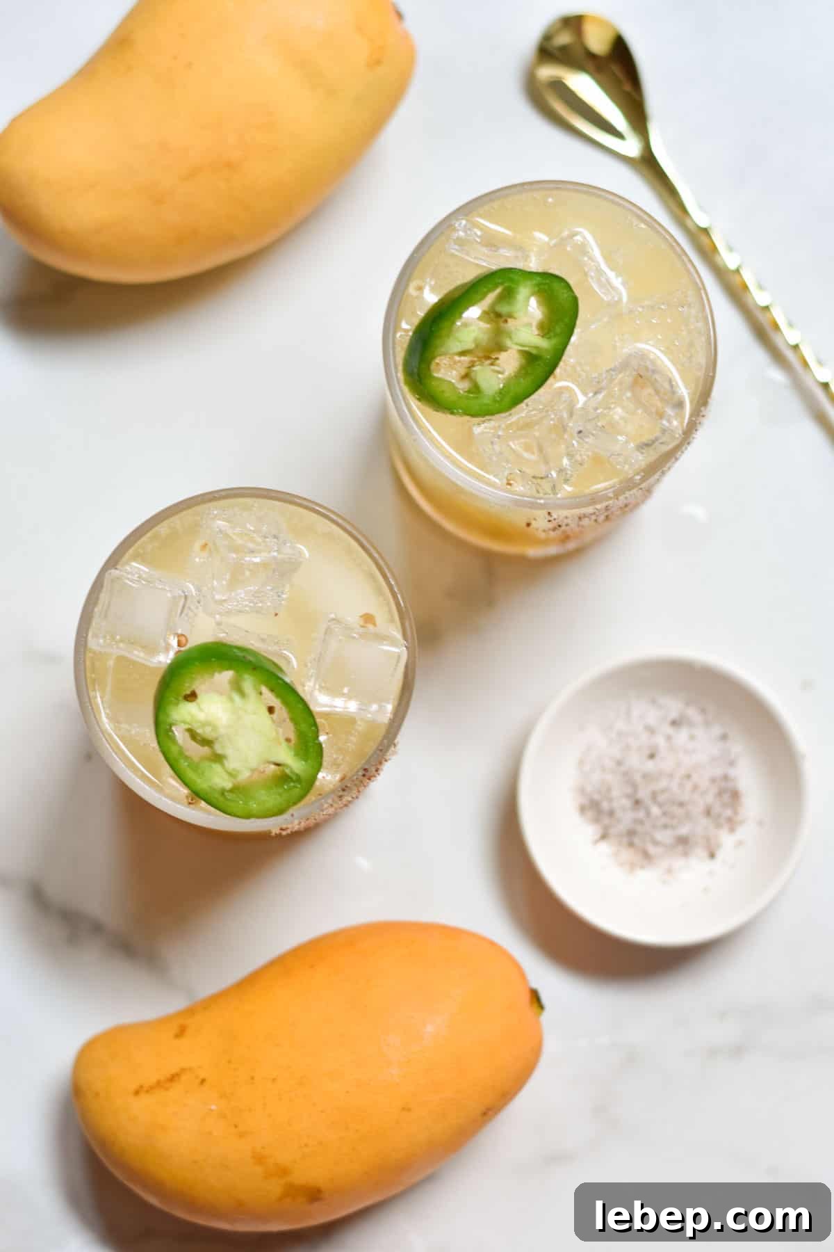 Two virgin margaritas next to fresh mangoes and salt with a mixer.