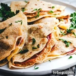 Savory Crepes: 10 Flavorful Fillings and Cooking Tips 11 A close-up of a plate stacked with savory crepes, folded and filled with what appears to be ham and cheese. The crepes are garnished with fresh parsley leaves, adding a touch of color to the dish.