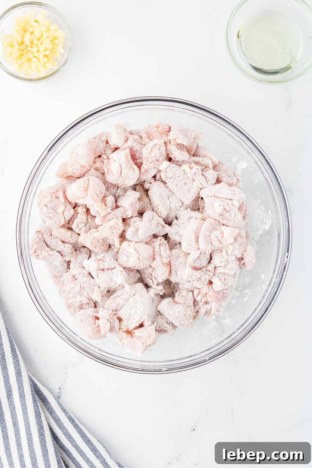 Chicken coated with cornstarch, salt, and pepper in a glass mixing bowl.