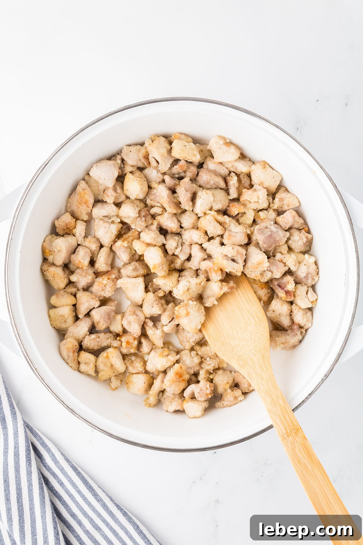 Diced chicken is seared in a large skillet until it is lightly golden brown.