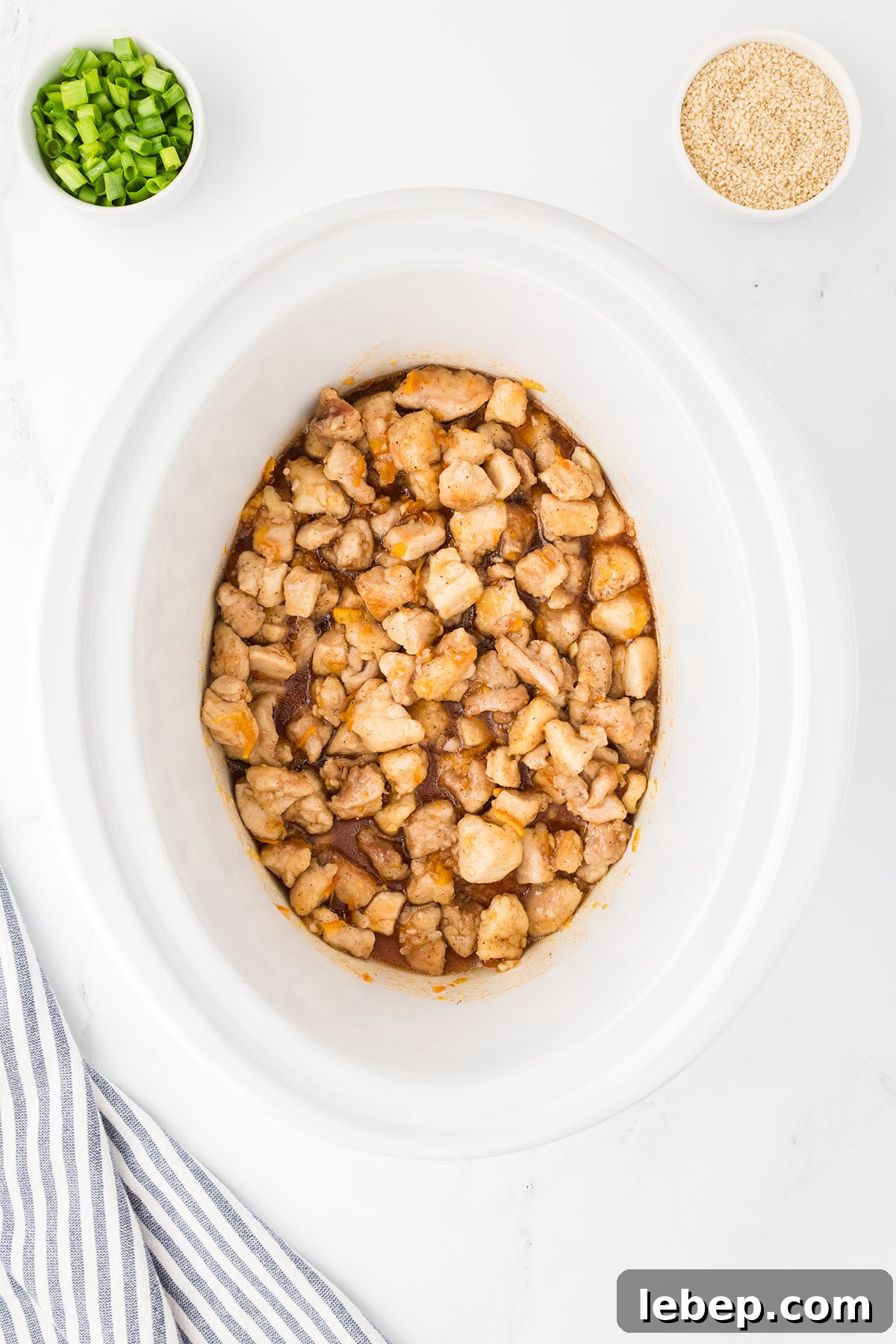 Chicken mixed with orange sauce in a slow cooker.