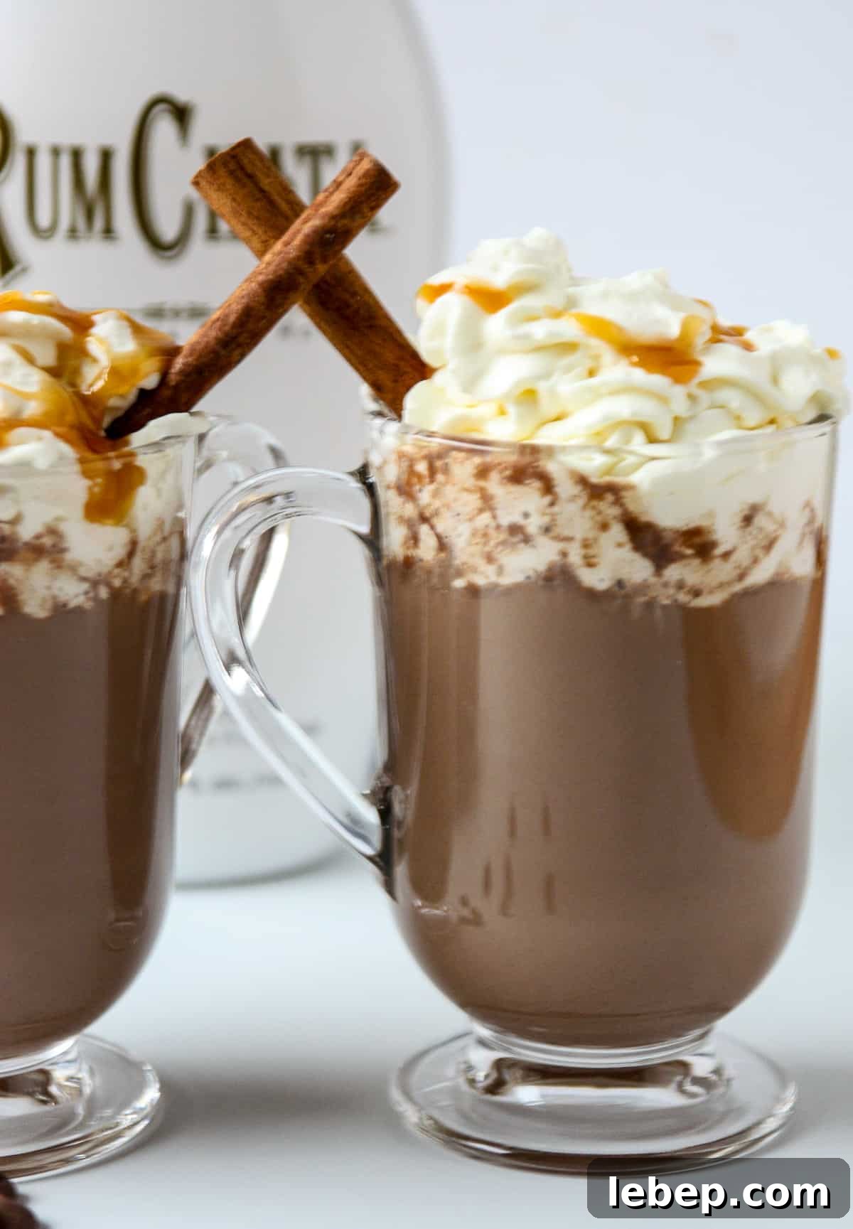 Warm RumChata Hot Chocolate Recipe: Creamy Spiked Cocoa for Chilly Nights 6 A bottle of RumChata behind two mugs of hot chocolate.