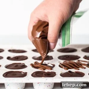 Peanut Butter Twix Cups Recipe — Homemade Candy Bars in Minutes 12 A person is dipping chocolate into a tray of cupcakes.