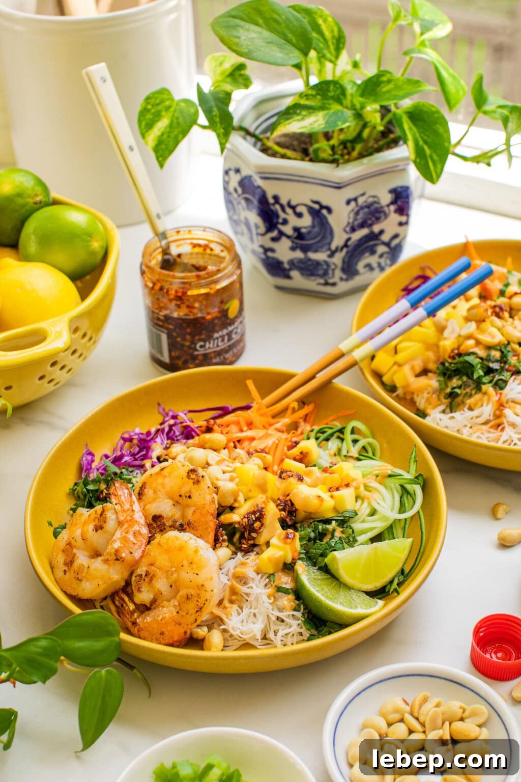 Spring Roll Bowl Recipe: Fresh Vietnamese Salad Bowl with Dipping Sauce 9 spring roll ingredients in a bowl covered with peanut sauce and grilled shrimp, surrounded by bowls of ingredients and a chili sauce in the background