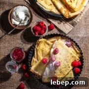 Pandekager folded in triangles in a black, round backing dish, served with raspberries, icing sugar, jam and cream.