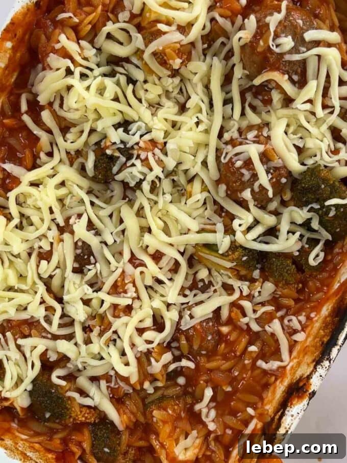 How to make Meatball Orzo Bake, step 4. Cheese is sprinkled over the dish with orzo, meatballs and broccoli in a tomato sauce.