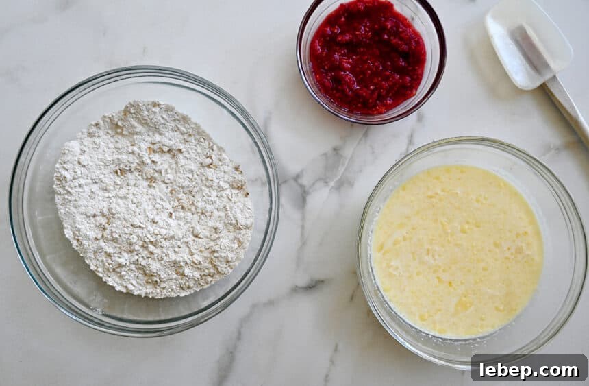 Fluffy Raspberry Oat Pancakes with Maple Glaze 3 A top-down view of three bowls containing wet and dry ingredients and mashed berries