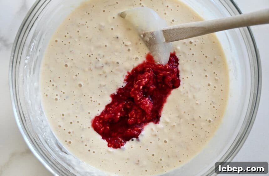 Fluffy Raspberry Oat Pancakes with Maple Glaze 4 Mashed berries being stirred into batter with a spatula