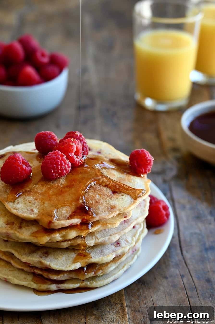Fluffy Raspberry Oat Pancakes with Maple Glaze 6 A tall stack of Raspberry Oatmeal Pancakes topped with maple syrup and fresh raspberries
