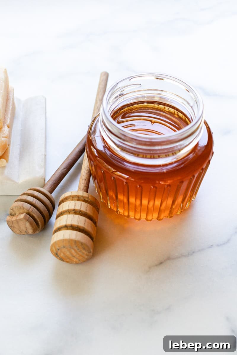 A jar of local honey with two honey combs on a white marble table. 