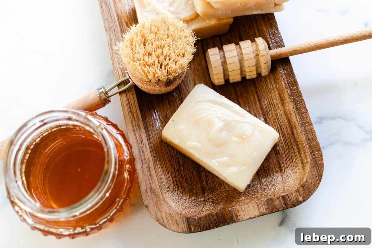 Scrub brush, honey, and a honey comb on a wooden bath tray.