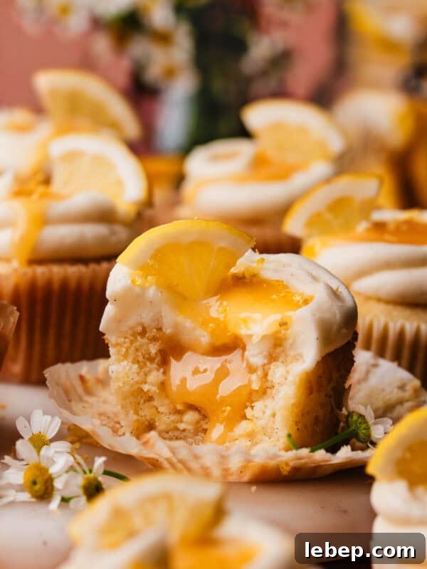 Key Lime Pie Cookies with Make-Ahead Prep Tips 11 A lemon cupcake on a marble cake plate, surrounded by more lemon cupcakes. The one in focus has bites missing, to show the lemon curd filling inside.