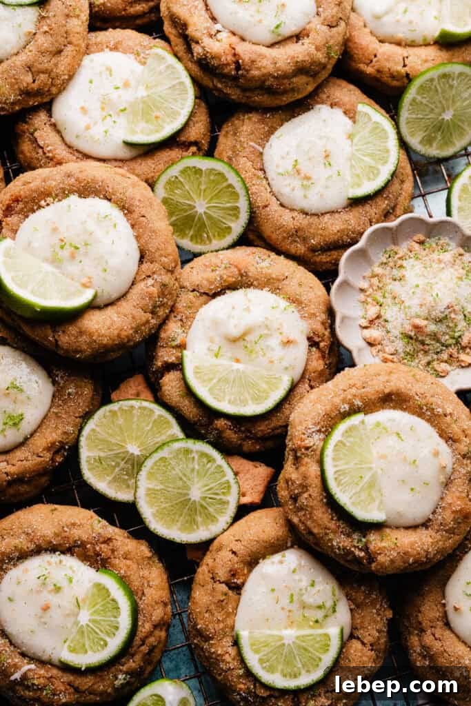 Key Lime Pie Cookies with Make-Ahead Prep Tips 9 Key Lime pie cookies nestled together on a cooling rack, with slices of lime for garnish scattered around.