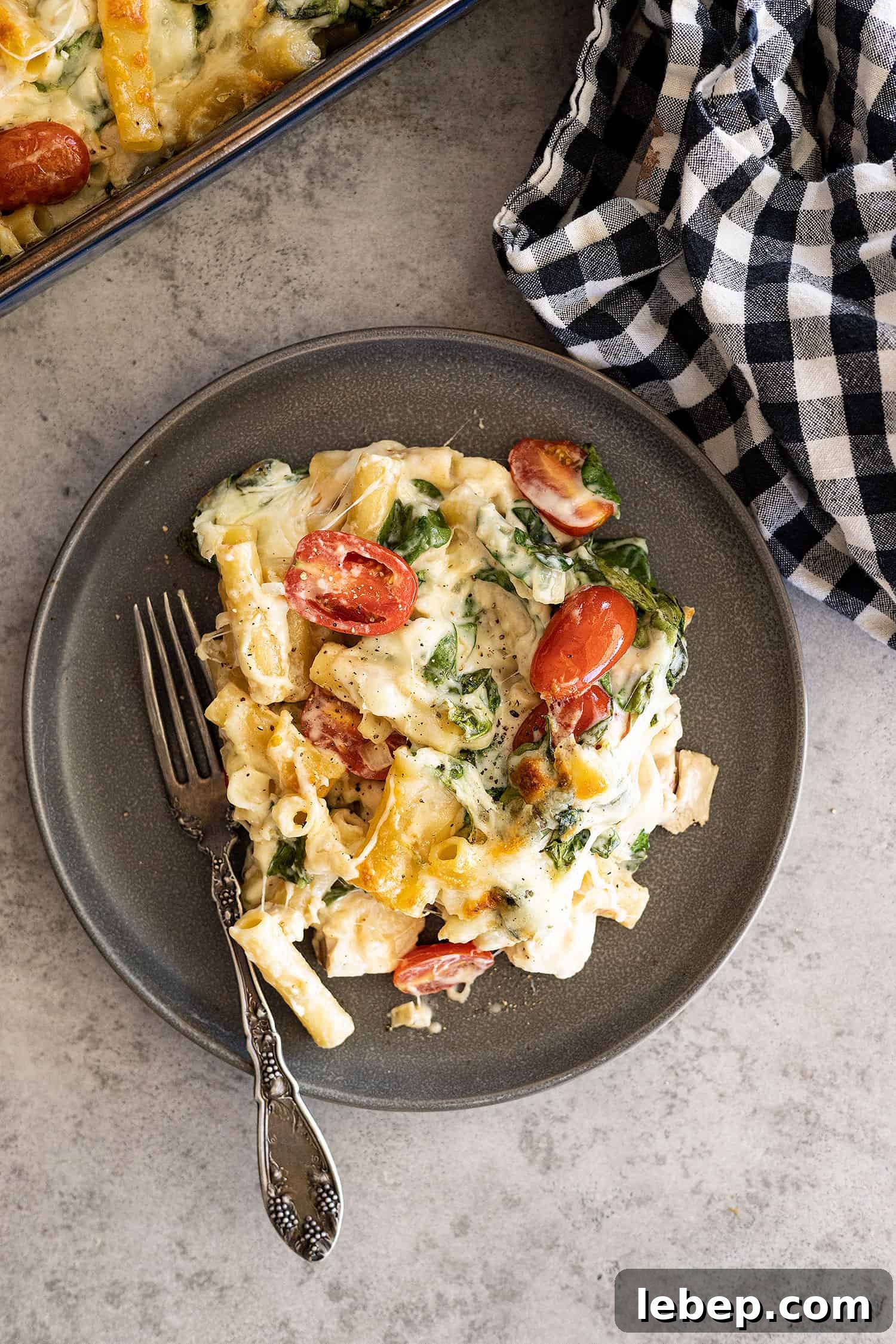 Creamy Chicken Florentine Pasta Bake Recipe 2 Overhead of casserole on a dark plate with fork off to the side.