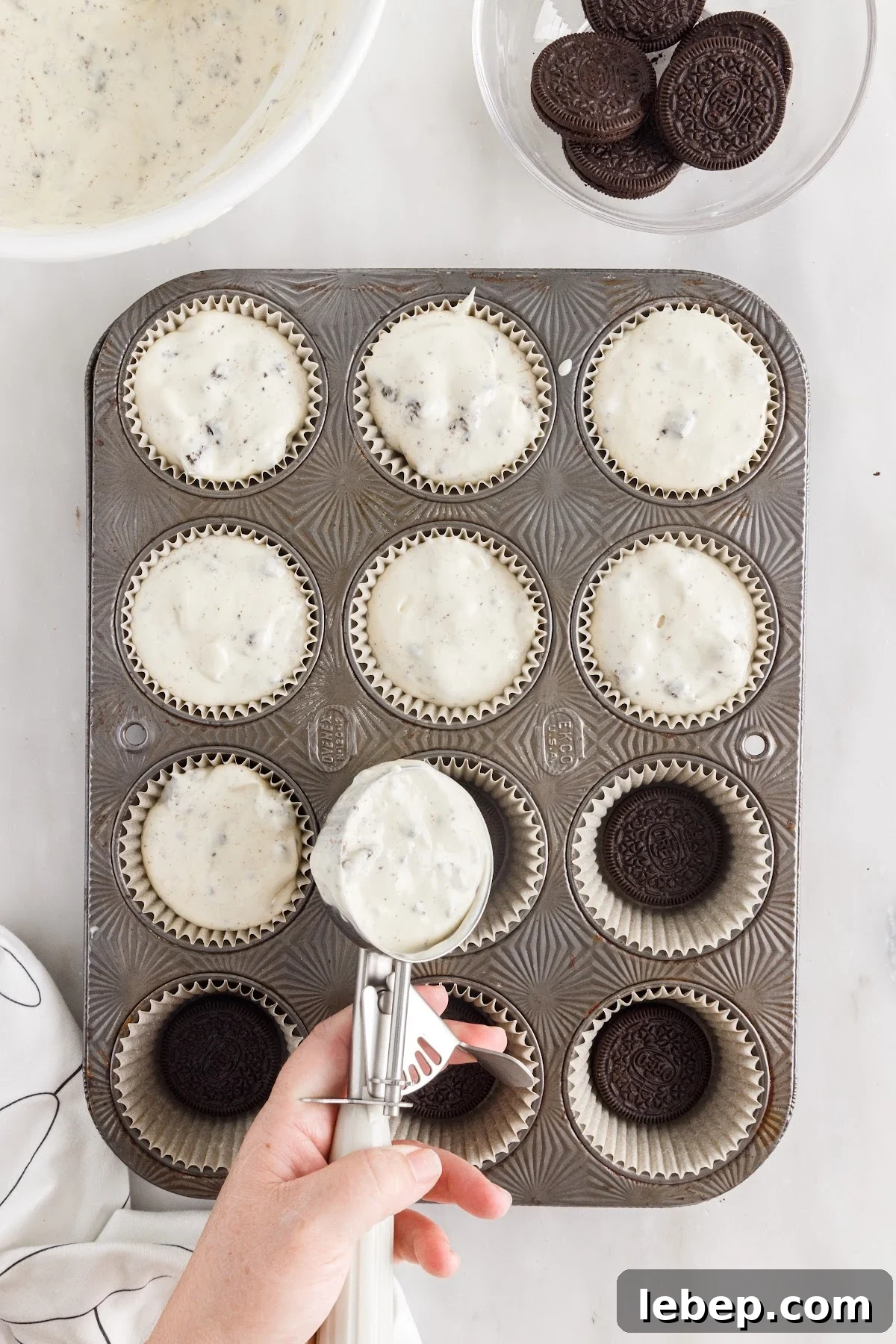 Scooping the cheesecake mixture into the prepared muffin liners.