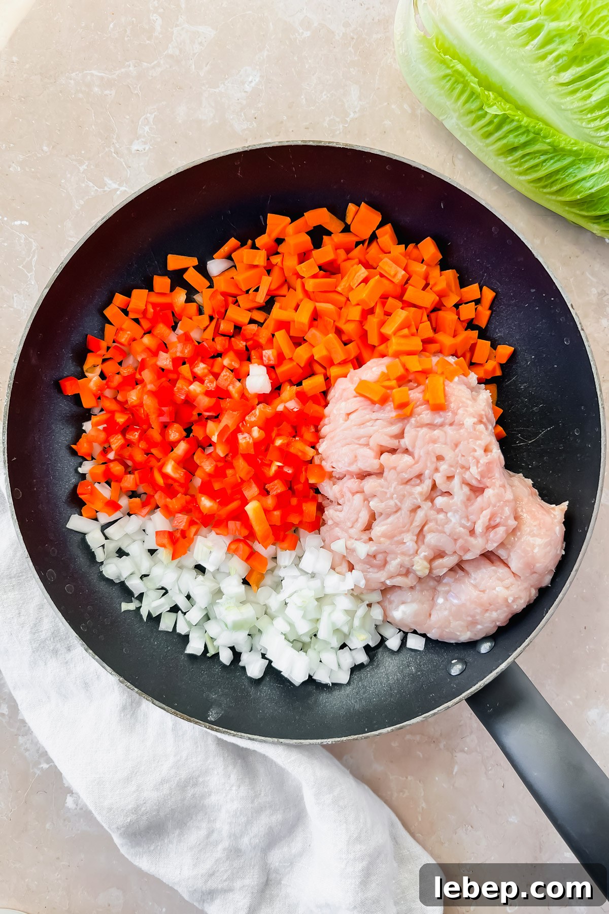 raw ground chicken, diced red pepper, carrots and white onion in black skillet.